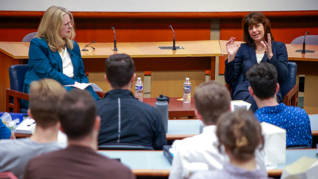 Abrams and Prelogar sitting across from each other at the front of a large class