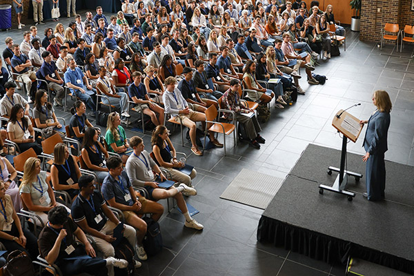 large group of students are seated in an open room facing a stage where Dean Kerry Abrams speaks