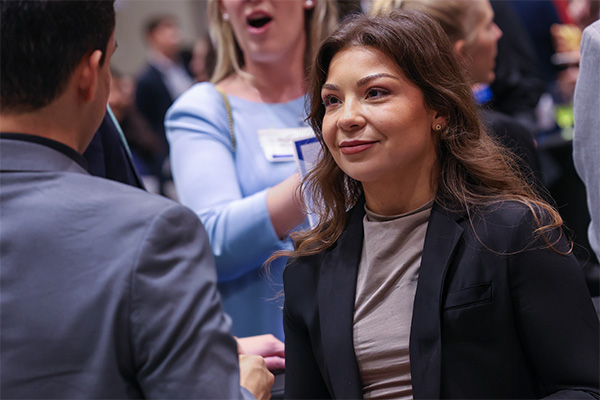 woman wearing a blazer talks to another person whose back is to the camera